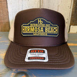 Brown and khaki high crown trucker hat with mesh back, adjustable snap closure, suitable for casual outdoor wear.