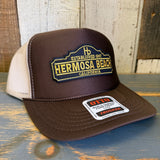 Brown and khaki high crown trucker hat with mesh back, displayed on a rustic wooden surface.