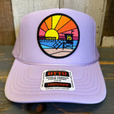 Lavender trucker hat with mesh back, featuring a sunset pier patch on the front. Ideal for casual, outdoor wear.
