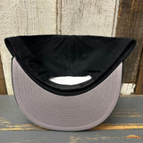 Black 6-panel snapback hat, inside out, displayed on a rustic wood surface. Fabric and stitching details are visible.