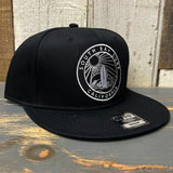 Black 6-panel snapback hat with round patch featuring surfboard, sun, and waves; suitable for casual or beachwear.