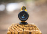 Yellow 8X monocular telescope rests upright on a weathered wooden post, lens directed toward the viewer.