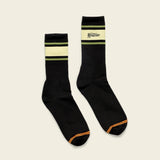 Black cotton crew socks with green and yellow stripes, orange toes, and logo text. Designed for everyday wear.
