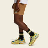 Person wears tan shorts, white crew socks with logo, and yellow-green mesh sneakers against a simple background.