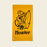 Yellow towel with a monkey holding a surfboard and 'Howler' branding on a beige background.