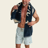 Man holding a navy beach towel with white patterns on a beige background.