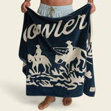 Person holding a navy blue towel with white text and graphics on a beige background.