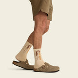 Person wearing beige socks with a logo, standing on a light background.