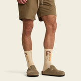 Person wearing beige socks with text, brown shorts, and shoes on a light background.