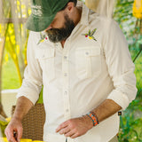 A man wearing a white shirt with bird designs and a green cap outdoors.