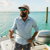 Man on a boat in sunglasses and cap wears a light blue, long sleeve tech shirt suited for outdoor water activities.