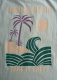 Aqua organic cotton pocket tee with sun, palm, and wave graphic; Take It Easy text at the hem.