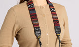Tan buttoned sweater and woven tapestry camera and binoculars strap worn around neck.