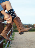 Individual sitting on a fence in brown leather cowboy boots, denim shorts, and patterned white crew socks.