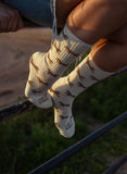 Person sitting on a fence outdoors wearing cotton socks with a brown horse print, paired with denim shorts.
