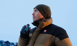 Person in a winter jacket and beanie uses a black waterproof monocular while holding a vape outdoors.