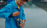Person in a blue raincoat holding a camera near water