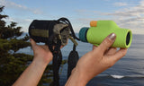 Person holding a green and black binoculars against a scenic ocean backdrop