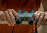 Hands grip waterproof binoculars with a yellow logo, featuring a metal bar for stability and outdoor use.