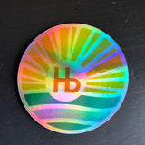 Holographic sticker with a sunburst design and bold Hb letters, ideal for personalizing laptops or water bottles.