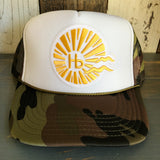 Camo/khaki/olive/white mesh trucker hat with yellow sunburst and wavy graphic logo on the front.