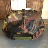 Camouflage trucker hat with mesh snapback, shown from the back, resting on a wooden surface.