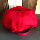 Black and red 5-panel high crown cap displayed on dark wood against a rustic background, for casual everyday wear.