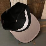 Black 6-panel snapback hat flipped upside down to display interior brim and crown details.