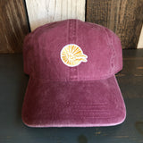 Maroon cotton dad hat with mini logo, displayed on a dark wooden surface.