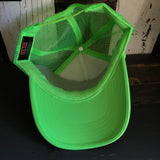 Neon green and white mesh trucker hat with classic logo, brim facing forward, displayed on a wooden surface.