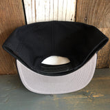 Black 5-panel snapback hat, fabric material, displayed upside down on a wooden surface.