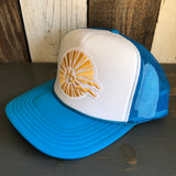 Neon blue and white trucker hat with classic logo, mesh back, displayed on a wooden surface.
