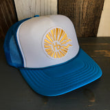 Neon blue and white trucker hat with sunburst HB logo, mesh back, displayed on a wooden surface.