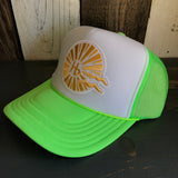 Neon green and white trucker hat with sunburst logo, mesh back, displayed on a dark wood surface.