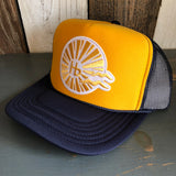 Navy and gold trucker hat with mesh back sits on a wooden surface, highlighting its classic style and casual use.