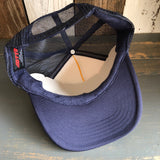 Navy and gold trucker hat displayed upside down, revealing mesh interior and adjustable strap for sizing.
