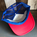 Red, white, and royal blue trucker hat shown upside down on a wooden surface, mesh back visible.