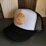 Black and white trucker hat featuring a yellow sunburst and hb logo, displayed on a wooden surface.
