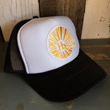 Black and white trucker hat with mesh backing, featuring a yellow sun and HB logo on the front.