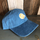 Blue cotton baseball cap with yellow sun and wave embroidered patch on wooden table